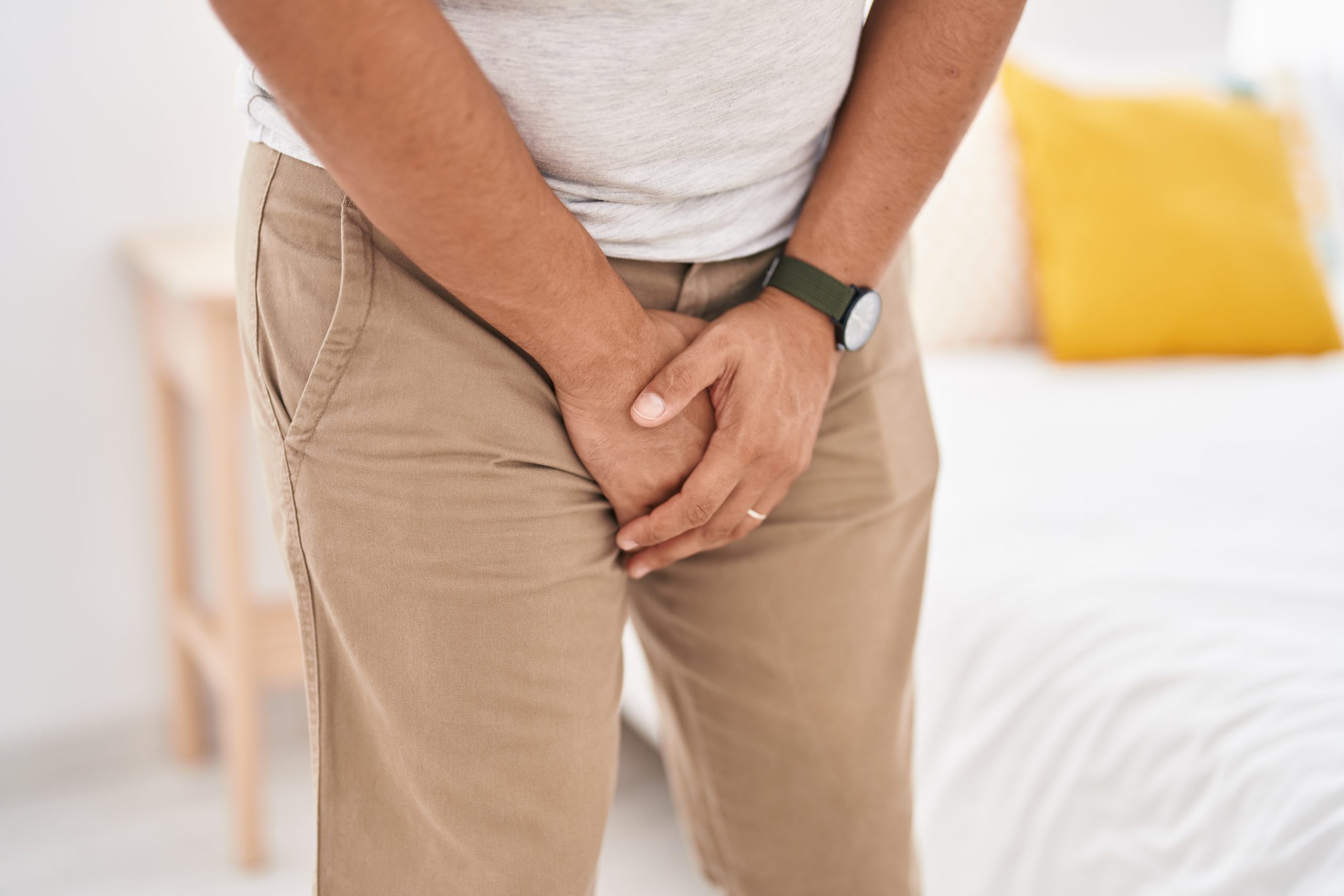 Young man covering his genitals with hands at bedroom